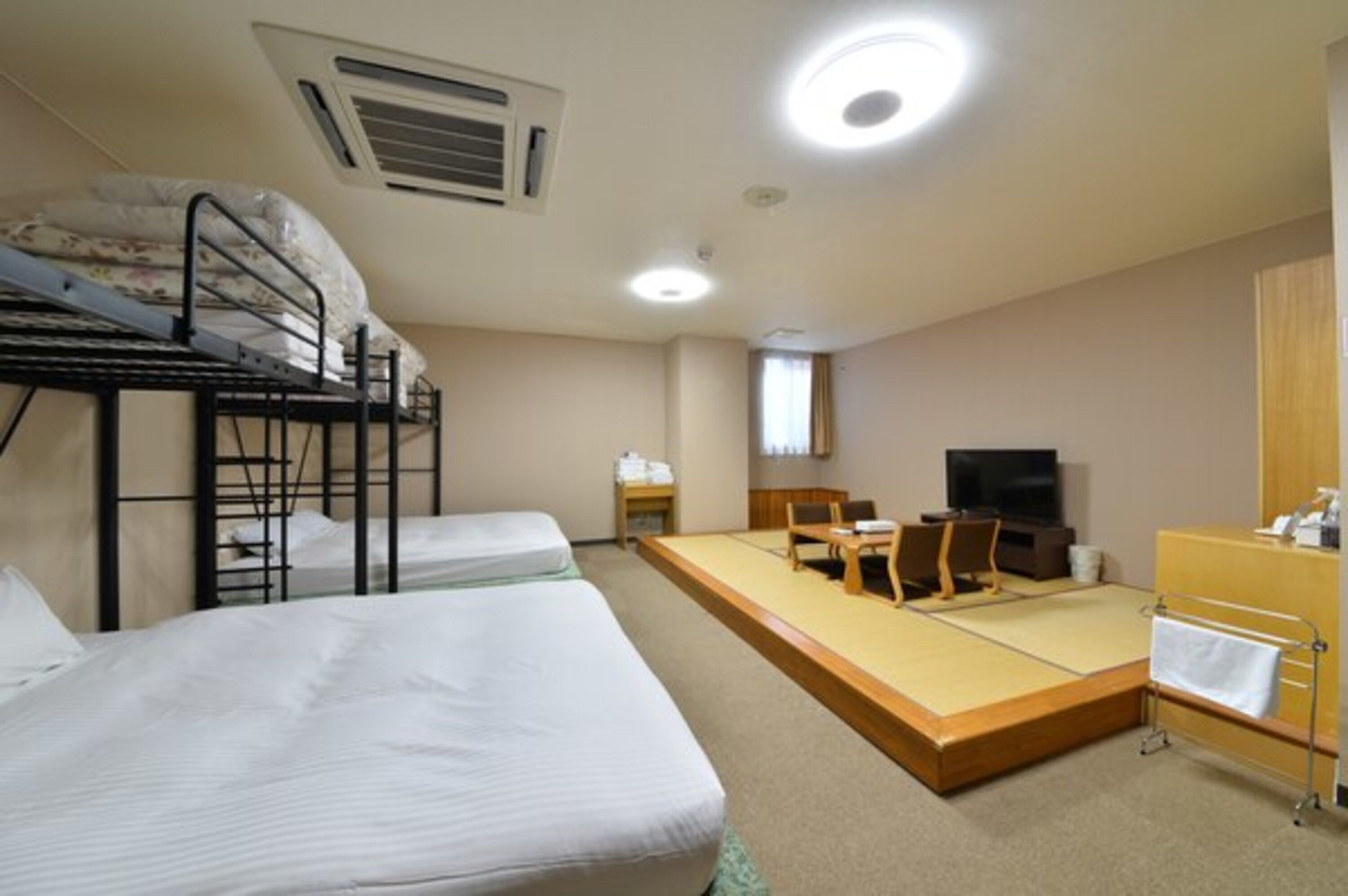 A dormitory room with bunk beds, a tatami mat area, a television, and a desk.