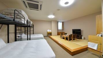 A dormitory room with bunk beds, a tatami mat area, a television, and a desk.