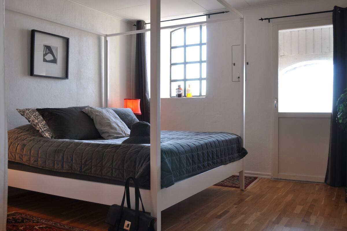 A bedroom with a bed, a window, a door, and a framed picture on the wall.