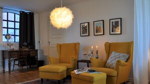 A living room with two yellow armchairs, a coffee table, a patterned rug, a chandelier, and framed pictures on the wall. - Villa Sandby Bed and Breakfast (Borrby)