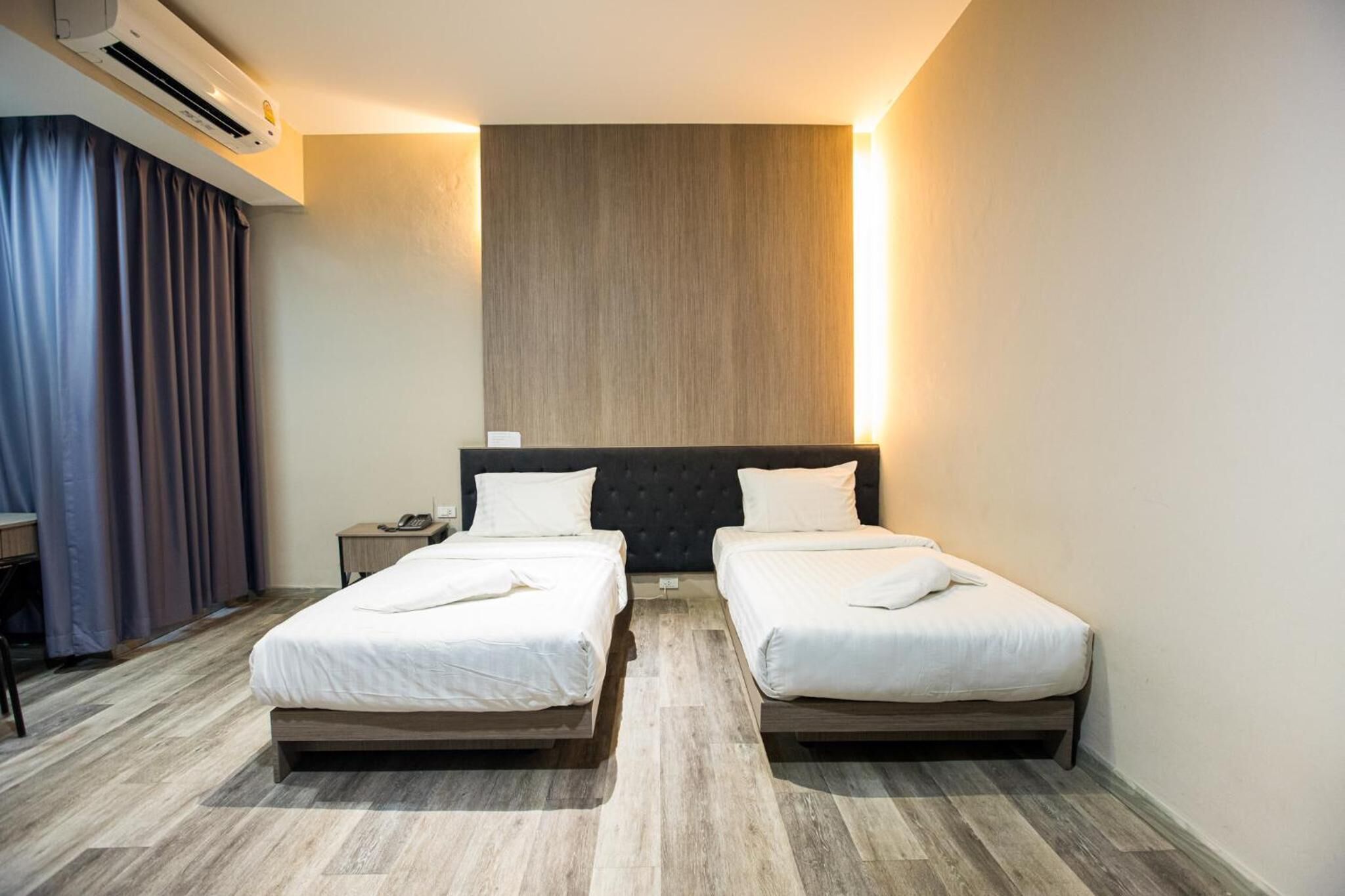 A hotel room with two single beds, a desk, a chair, an air conditioning unit, and a large wooden panel on the wall.