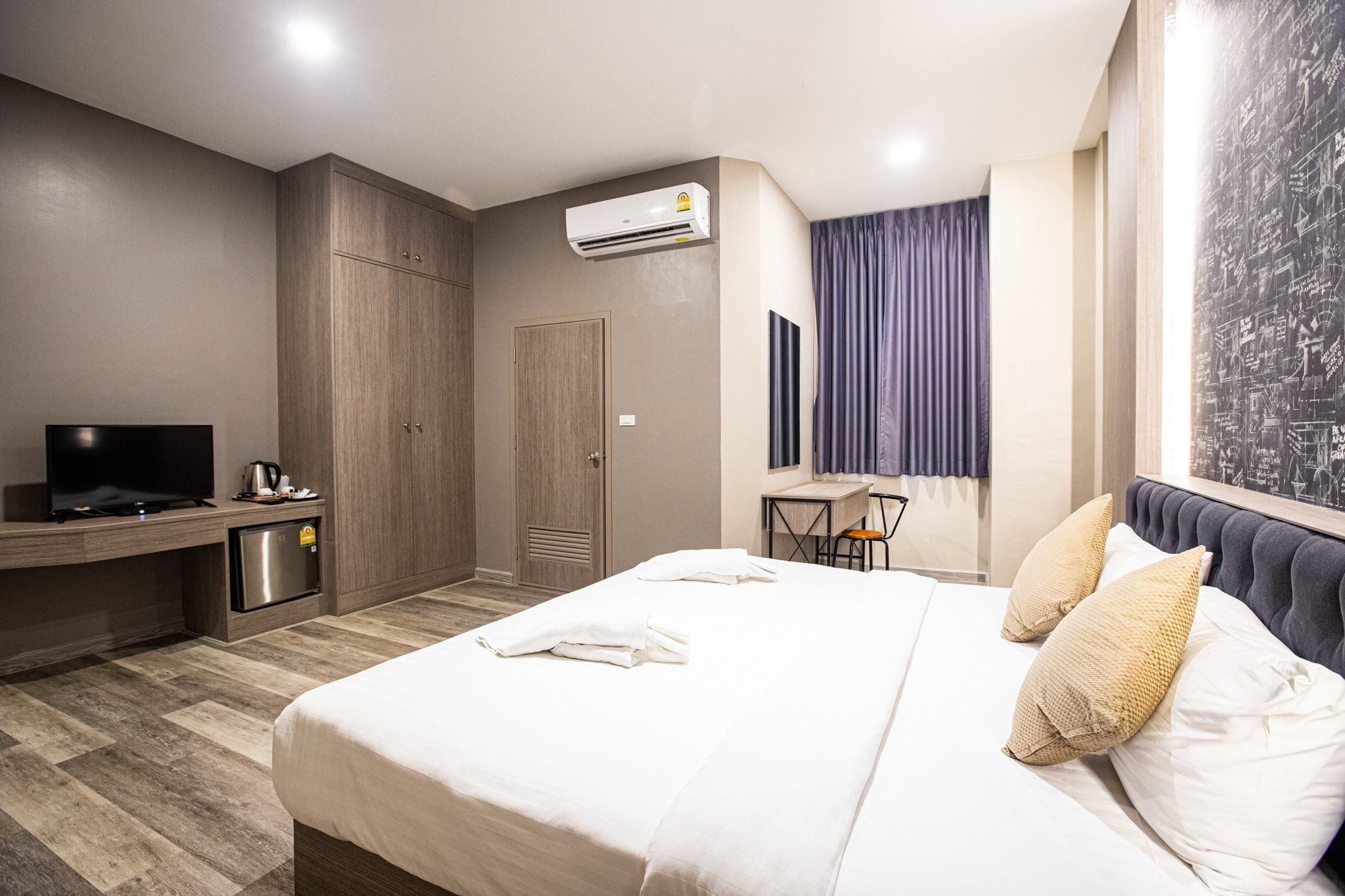 Ein Hotelzimmer mit Bett, Schreibtisch mit Fernseher, Minikühlschrank, Kleiderschrank und Klimaanlage.