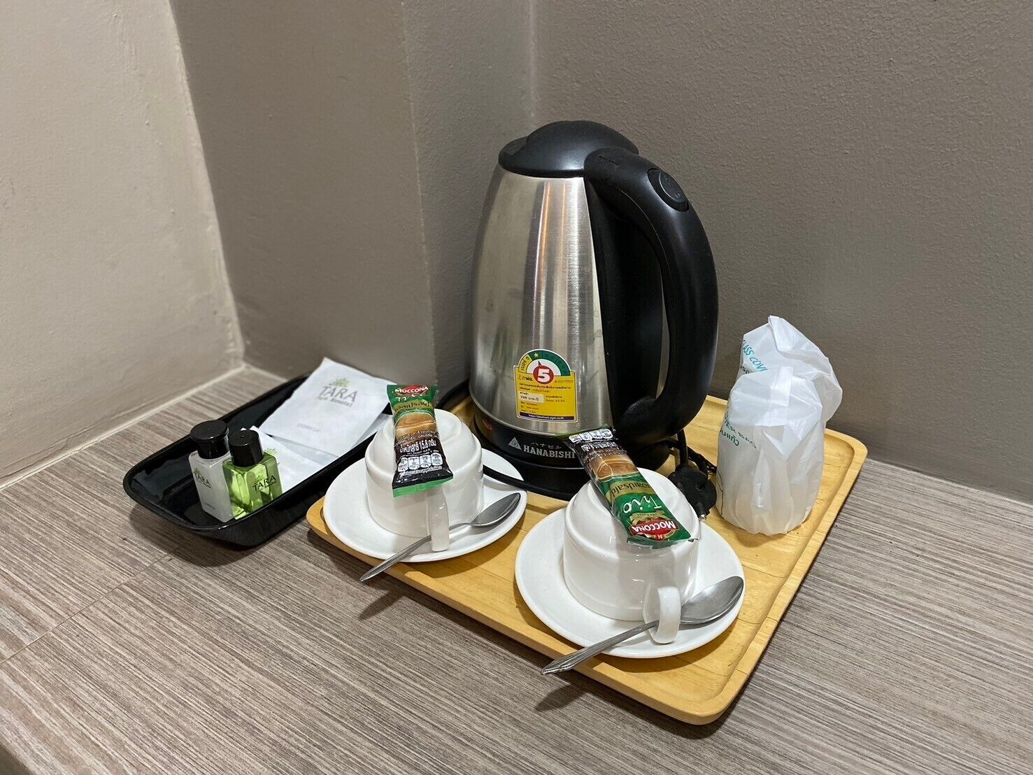 A breakfast setup with a coffee maker, two cups of tea, a tray with condiments, and a spoon.