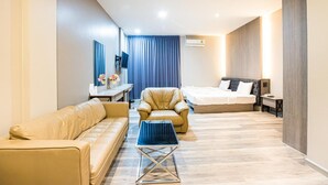A modern hotel room with a sofa, a chair, a small table, a bed, a desk, and a TV. - Tara Park Resotel (Thanyaburi)