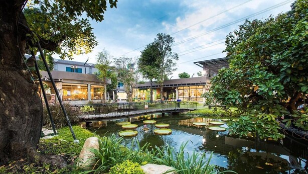 A serene garden with a pond, a wooden bridge, and buildings in the background. - Tara Park Resotel (Thanyaburi)