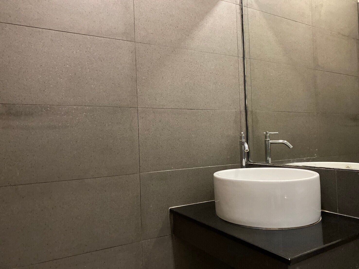A modern bathroom with a white sink, dark countertop, and grey tiled walls.