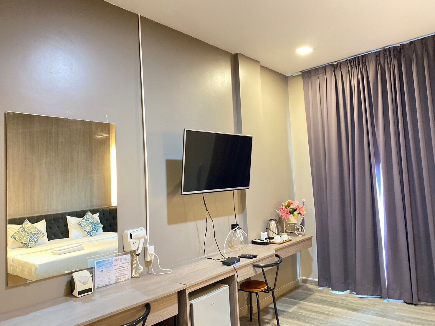 A modern hotel room with a large mirror, a flat-screen TV, a desk with a chair, and a large window with curtains.