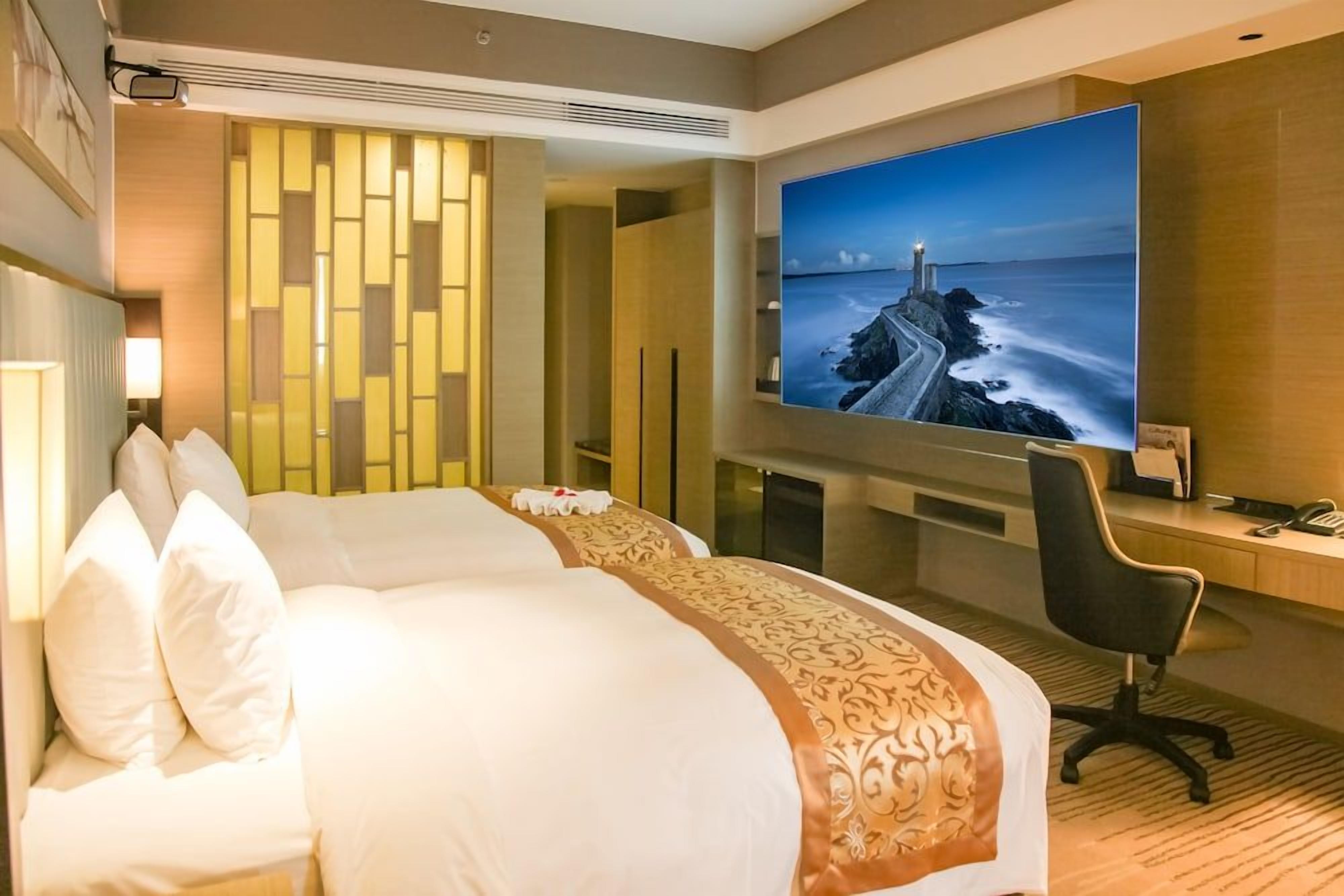 A hotel room with a large bed, a desk, a chair, and a television displaying a scenic view.
