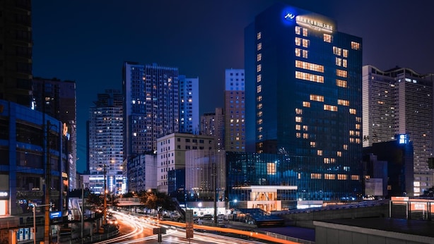 Ett högt hotell med upplysta fönster, en modern glasfasad och en framträdande logotyp högst upp.