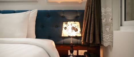 A hotel room with a bed, a nightstand with a lamp, a telephone, and a blue upholstered headboard.