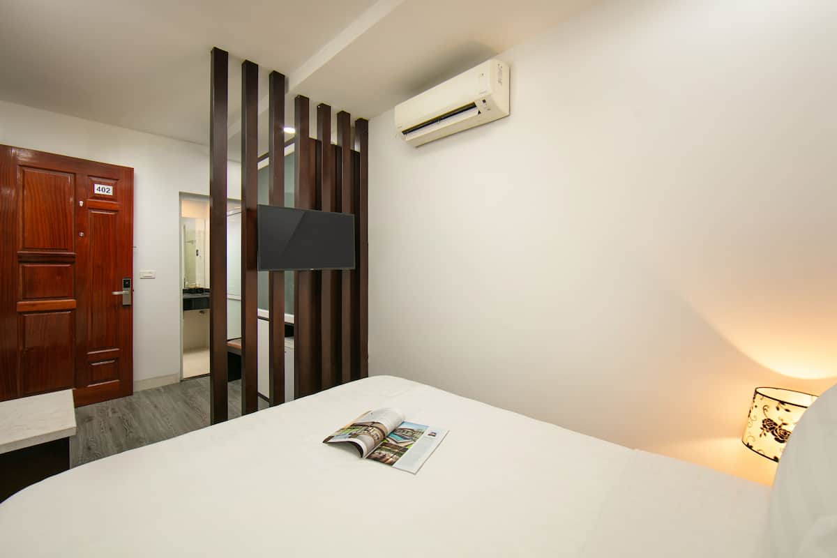 Habitación de hotel con cama, televisor montado en la pared, unidad de aire acondicionado y puerta de madera con el número 402.