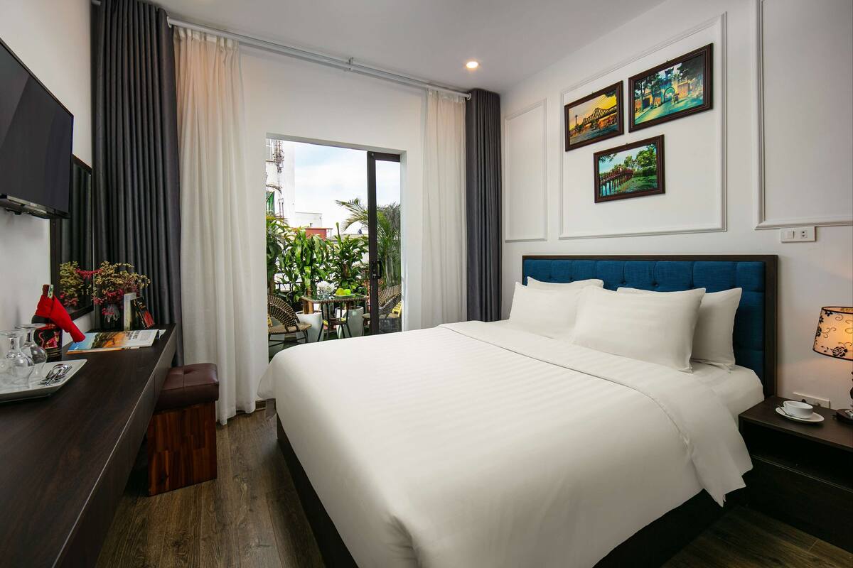 Habitación de hotel con una cama grande, un televisor, un escritorio y una sombrilla roja, y vistas a zonas verdes.
