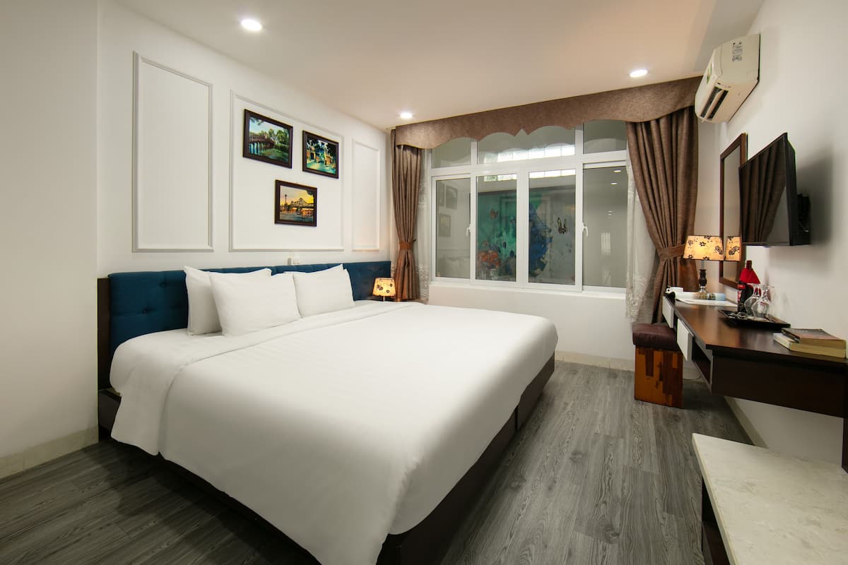 Una habitación de hotel con una cama grande, un escritorio con lámpara y una ventana con cortinas.