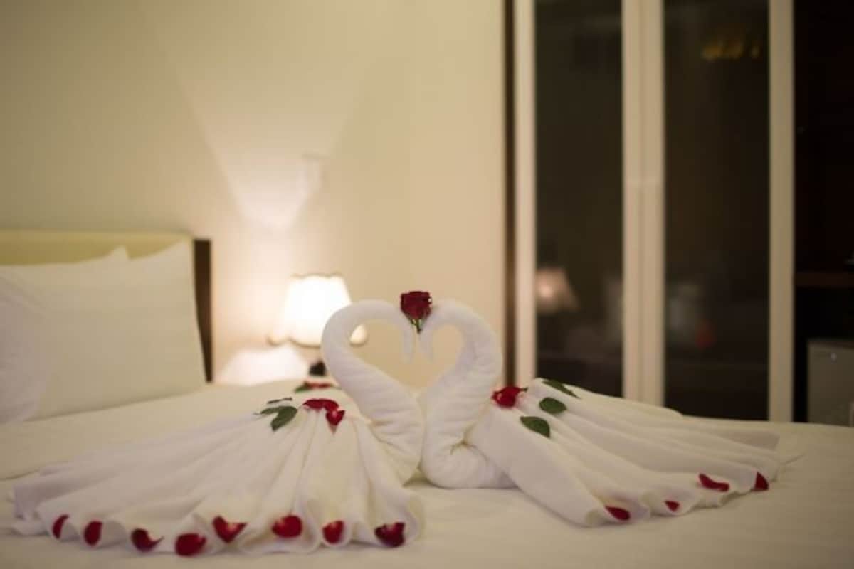A bed with white linens and a heart-shaped towel arrangement with roses.