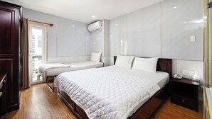 A hotel room with a large bed, a smaller bed, a wooden floor, a wardrobe, a nightstand, and an air conditioning unit. - Gia Hoa Hotel (Ho Chi Minh City)