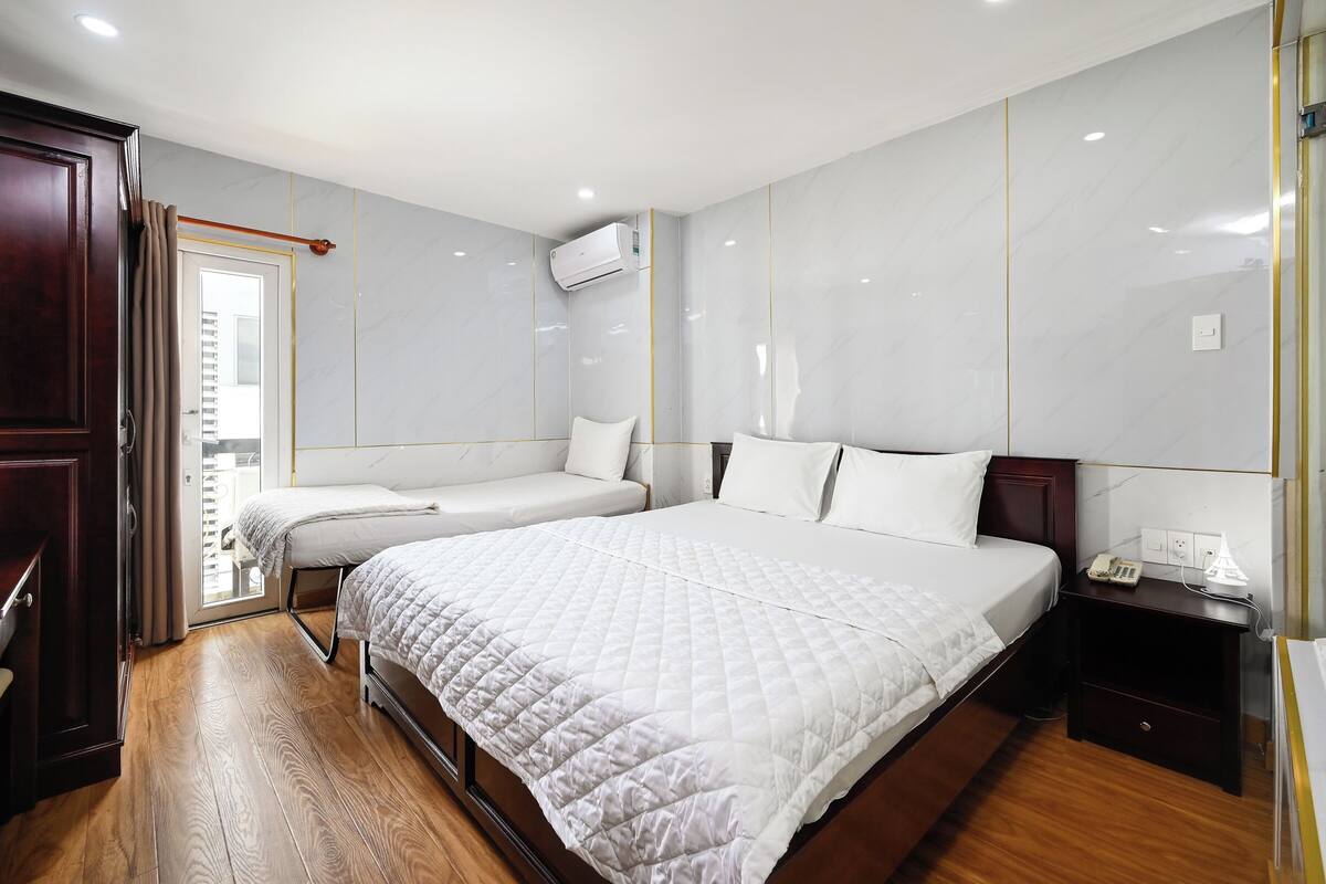 Une chambre d’hôtel avec un grand lit, un lit plus petit, un plancher en bois, une armoire, une table de chevet et un appareil de climatisation.