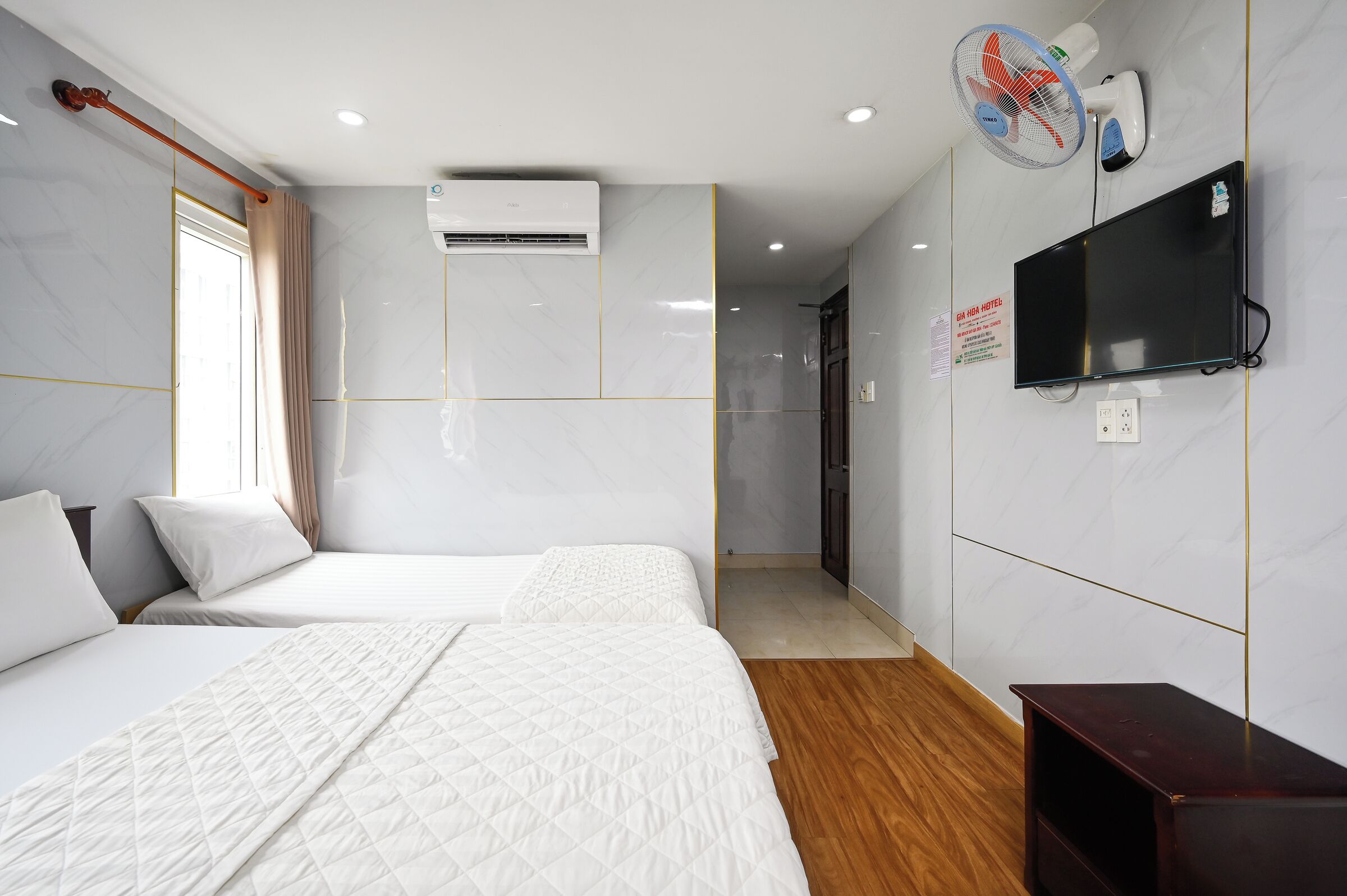 Une chambre d’hôtel avec deux lits, une télévision, un climatiseur et un ventilateur.