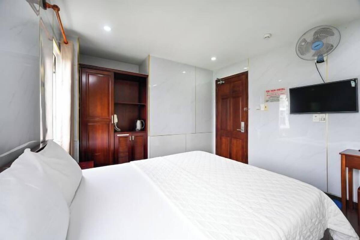 Une chambre d’hôtel avec un lit, une armoire en bois, un téléviseur et un ventilateur fixé au mur.