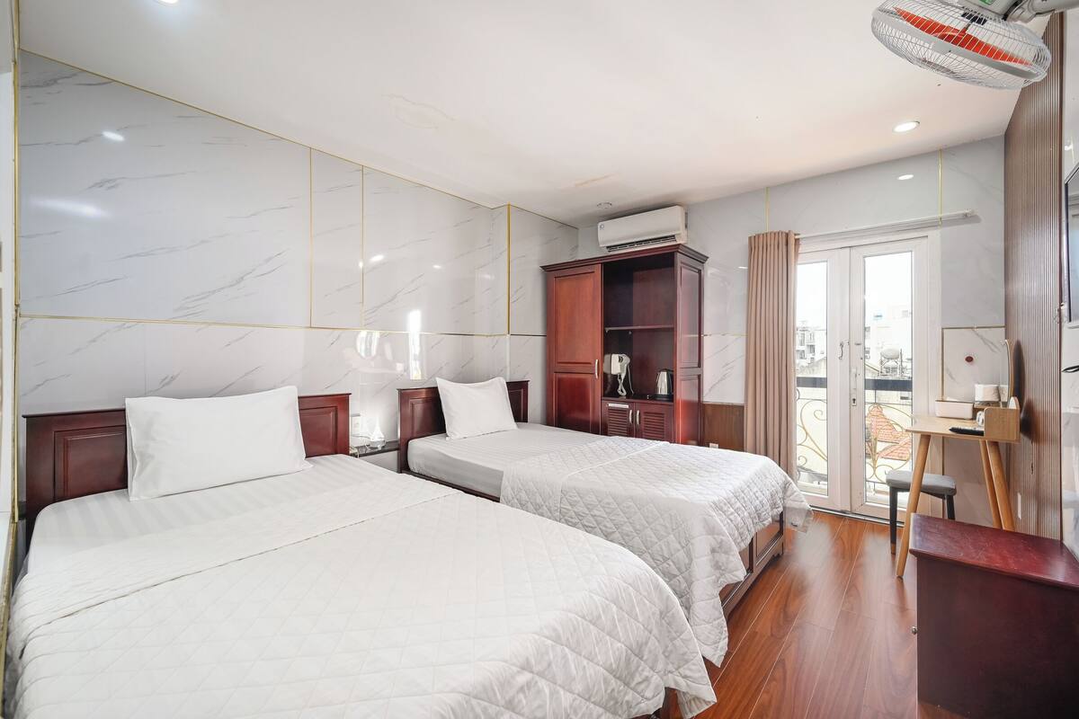 Une chambre d’hôtel avec deux lits, une armoire en bois, un appareil de climatisation et un bureau avec une chaise.
