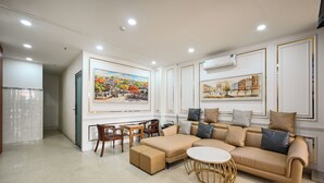A modern living room with a beige sectional sofa, a round coffee table, and a dining area with wooden chairs and a small table. - Gia Hoa Hotel (Ho Chi Minh City)