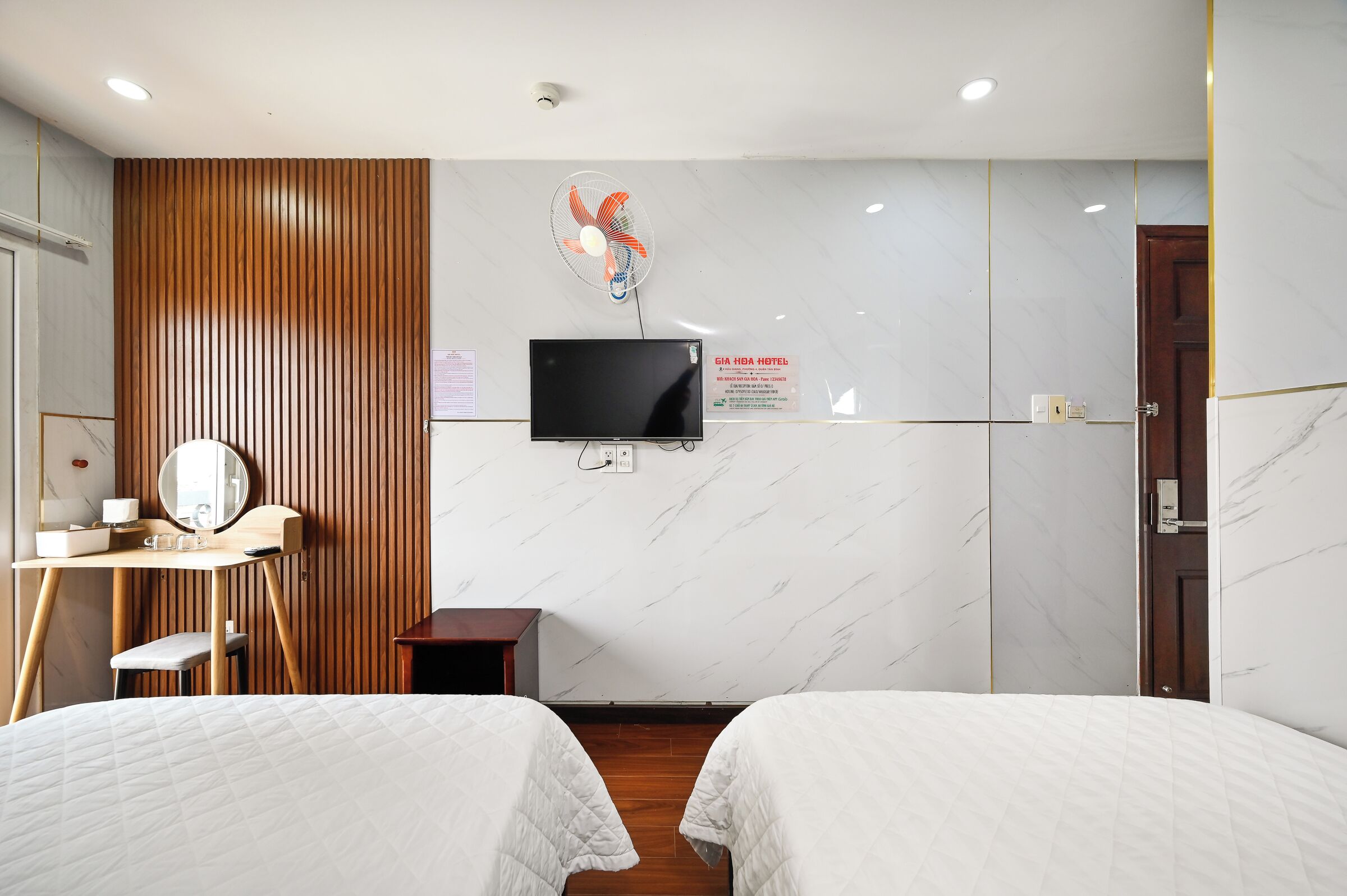 Une chambre d’hôtel avec deux lits, un bureau avec un miroir, une télévision et un mur recouvert de panneaux en bois.