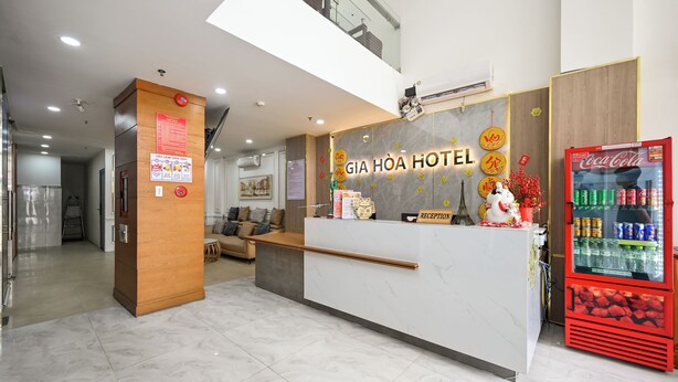 A hotel reception area with a marble floor, a reception desk, a Coca-Cola refrigerator, and a staircase in the background. - Gia Hoa Hotel (Ho Chi Minh City)