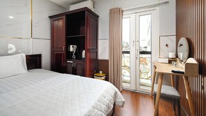 A hotel room with a bed, a wooden wardrobe, a desk with a chair, a mirror, and a balcony with a railing. - Gia Hoa Hotel (Ho Chi Minh City)