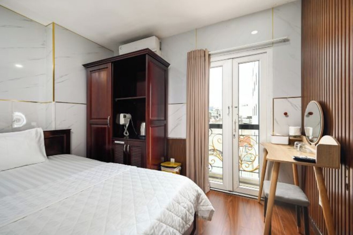 Une chambre d’hôtel comprenant un lit, une armoire en bois, un bureau avec une chaise, un miroir et un balcon avec une balustrade.