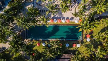 Eine Vogelperspektive auf einen Poolbereich, umgeben von Palmen, mit Liegestühlen und Sonnenschirmen rund um den Pool.