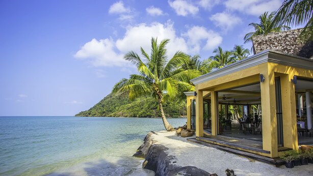 A beachside hotel with a covered outdoor seating area, a palm tree, and a view of the ocean. - Peninsula Beach Resort (Ko Chang)