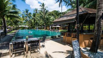 A pool area with lounge chairs and a bar, surrounded by palm trees.