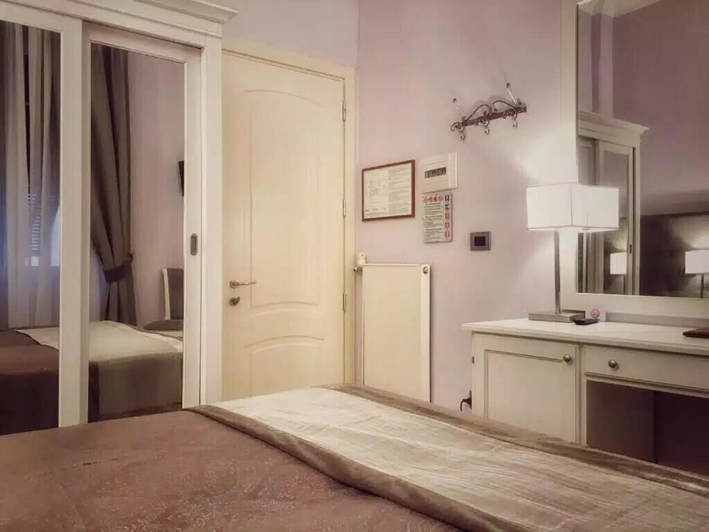 Quarto de hotel com cama, escrivaninha, espelho e porta.