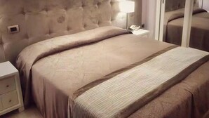 A bedroom with a tufted headboard, a bedside table with a lamp, and a mirror. - Hotel Villa Igea (Alassio)