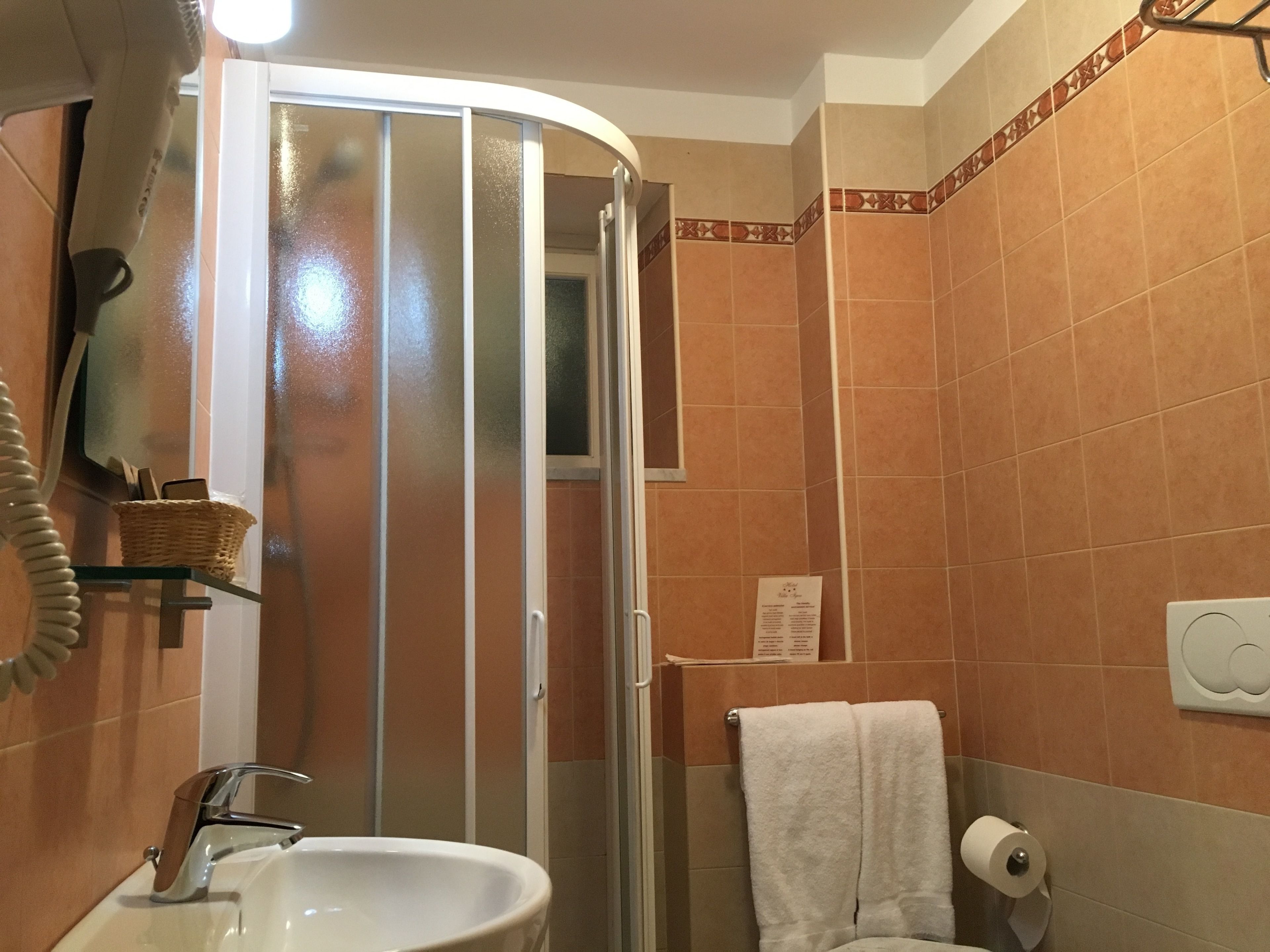 A bathroom with a glass shower enclosure, a sink, a towel rack, and a telephone.