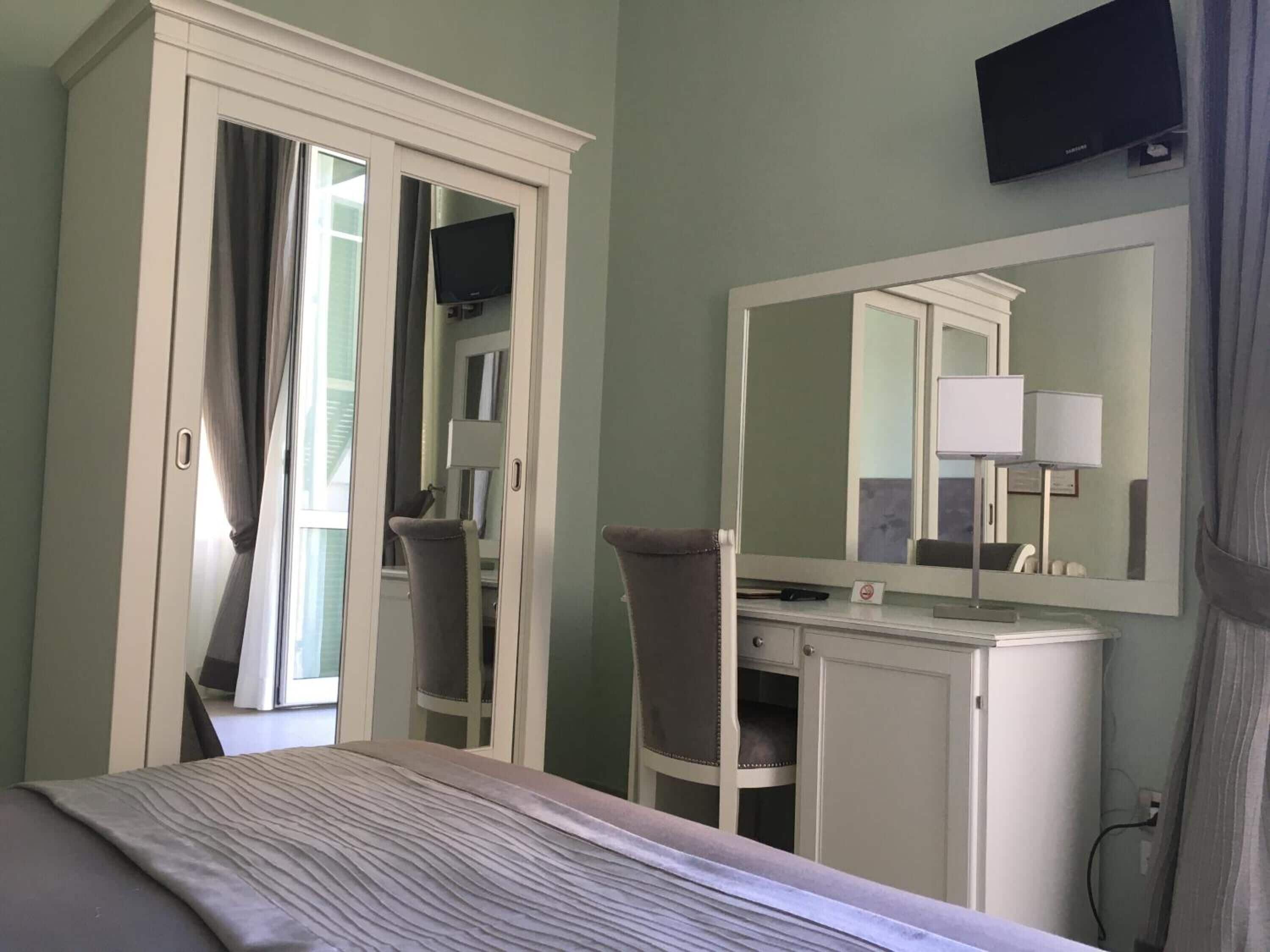 A hotel room with a bed, a desk, a chair, a wardrobe, a mirror, and a television.