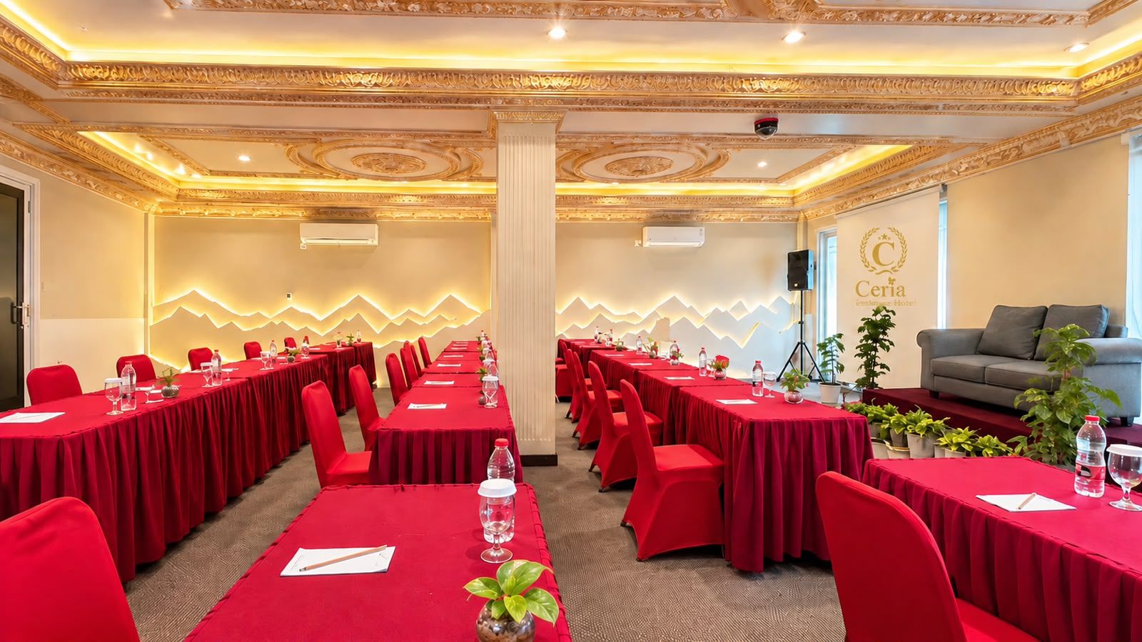 A conference room with rows of tables, red chairs, and a stage with a sofa.