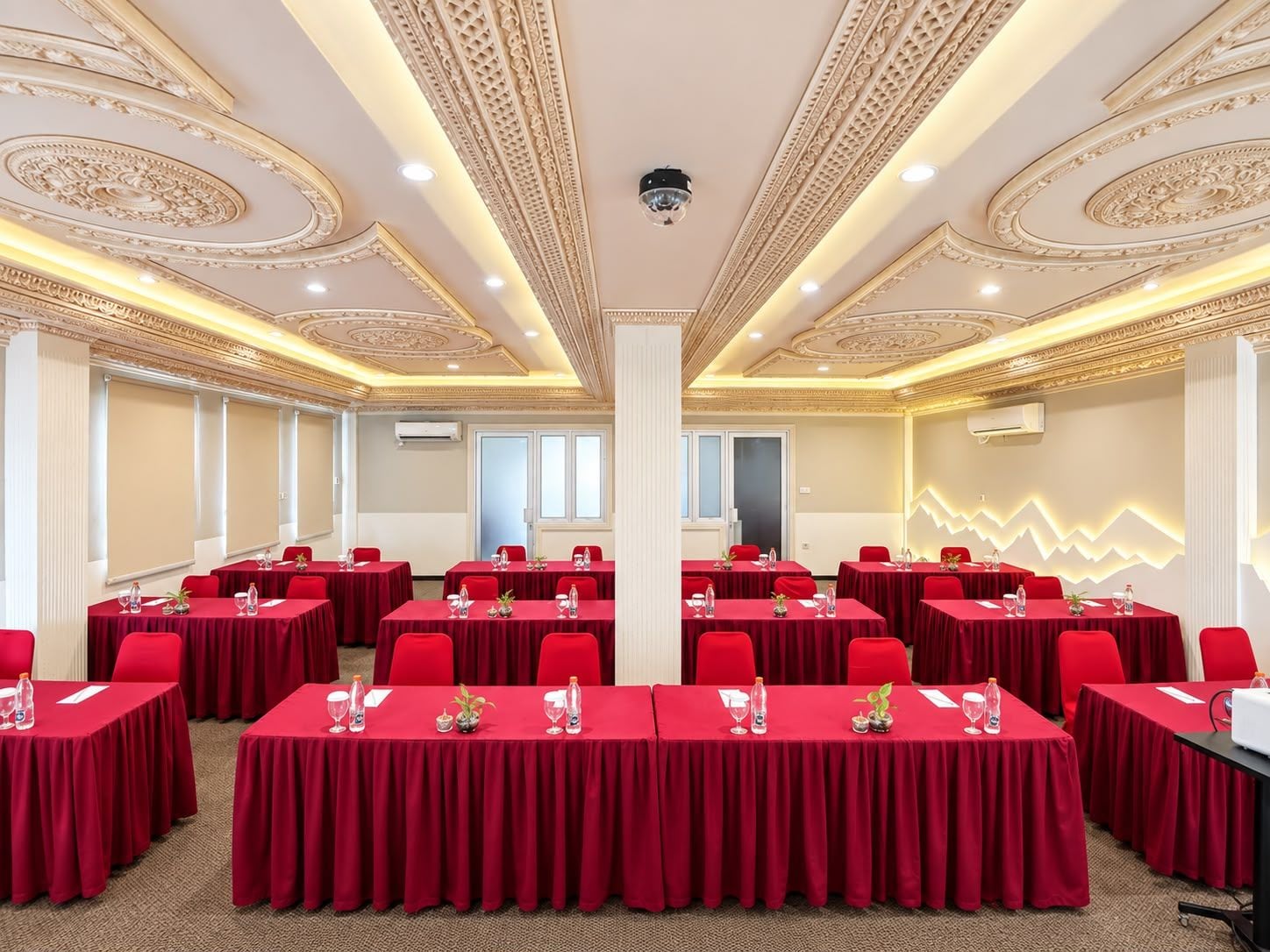 A conference room with red tables, white chairs, and ornate ceiling details.