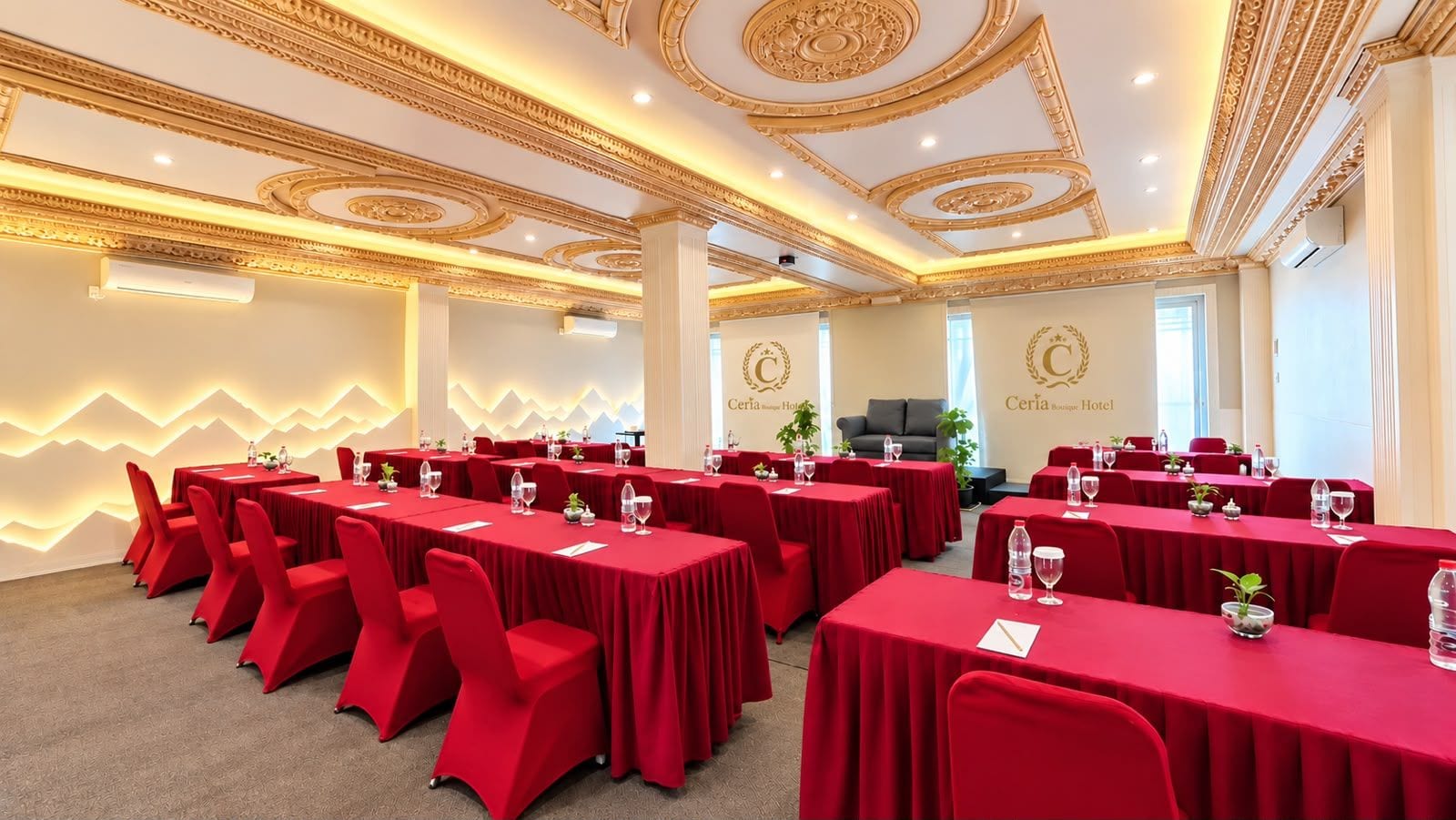 Un salón de conferencias con mesas y sillas rojas, un diseño de techo ornamentado y una decoración de pared con motivos de montaña.