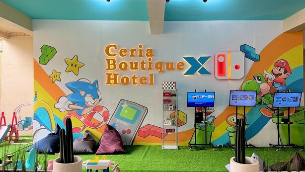 A colorful room with a mural of Sonic the Hedgehog, a gaming console, and Mario. There are three screens displaying content, a cactus plant, and a checkered shelf. - Ceria Boutique Hotel (Depok)