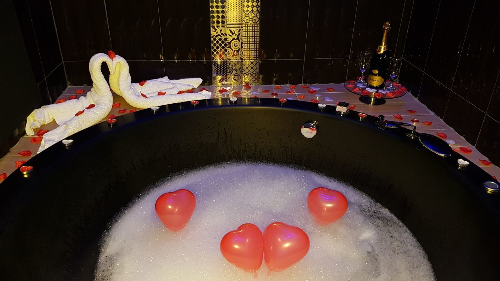 A bathtub with heart-shaped balloons and swan decorations, surrounded by a tiled wall with a patterned design.