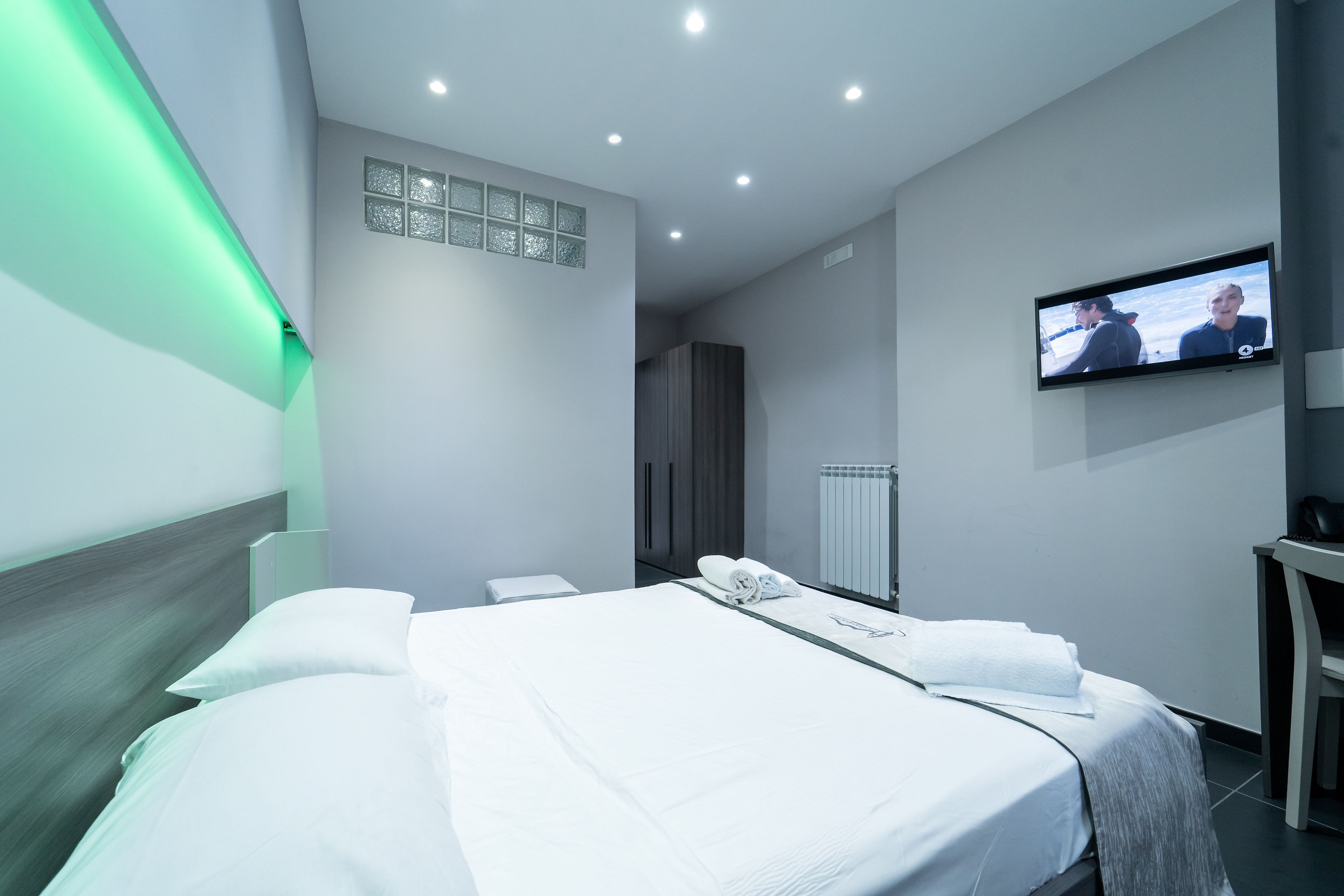A modern hotel room with a neatly made bed, a flat-screen TV mounted on the wall, and a small desk.