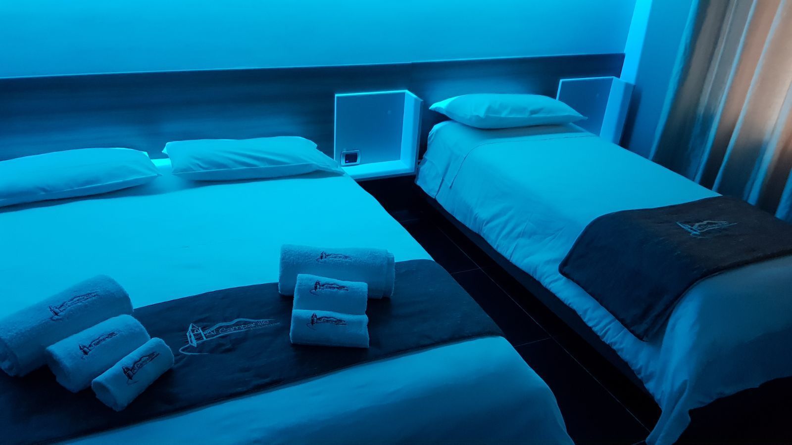 A hotel room with two beds, each with white linens and pillows. There are towels with embroidered text on the beds.
