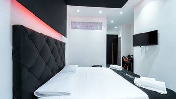 Una habitación de hotel moderna con una cama grande, un televisor de pantalla plana montado en la pared y un escritorio pequeño con una silla.