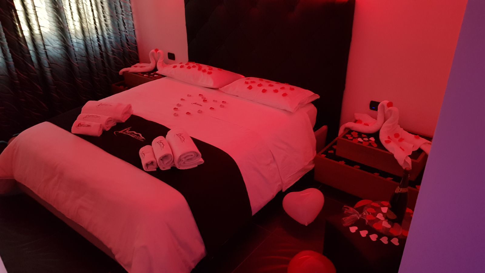 A bed with a heart-shaped pillow, a heart-shaped cushion, and a heart-shaped pillow on the nightstand.