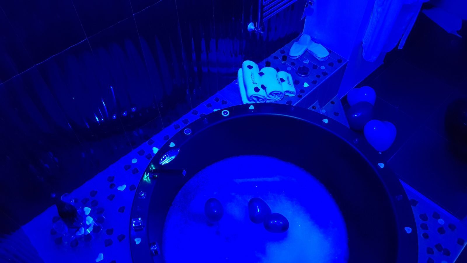 A blue-lit bathroom with a toilet, a sink, and a shower area.