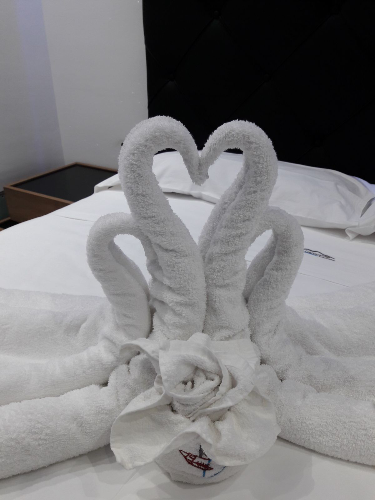 A neatly folded white towel with a heart-shaped design on a bed.