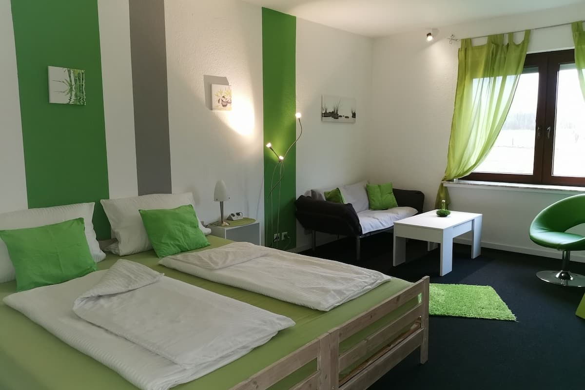 A room with two beds, a small table, a chair, and a window with curtains.