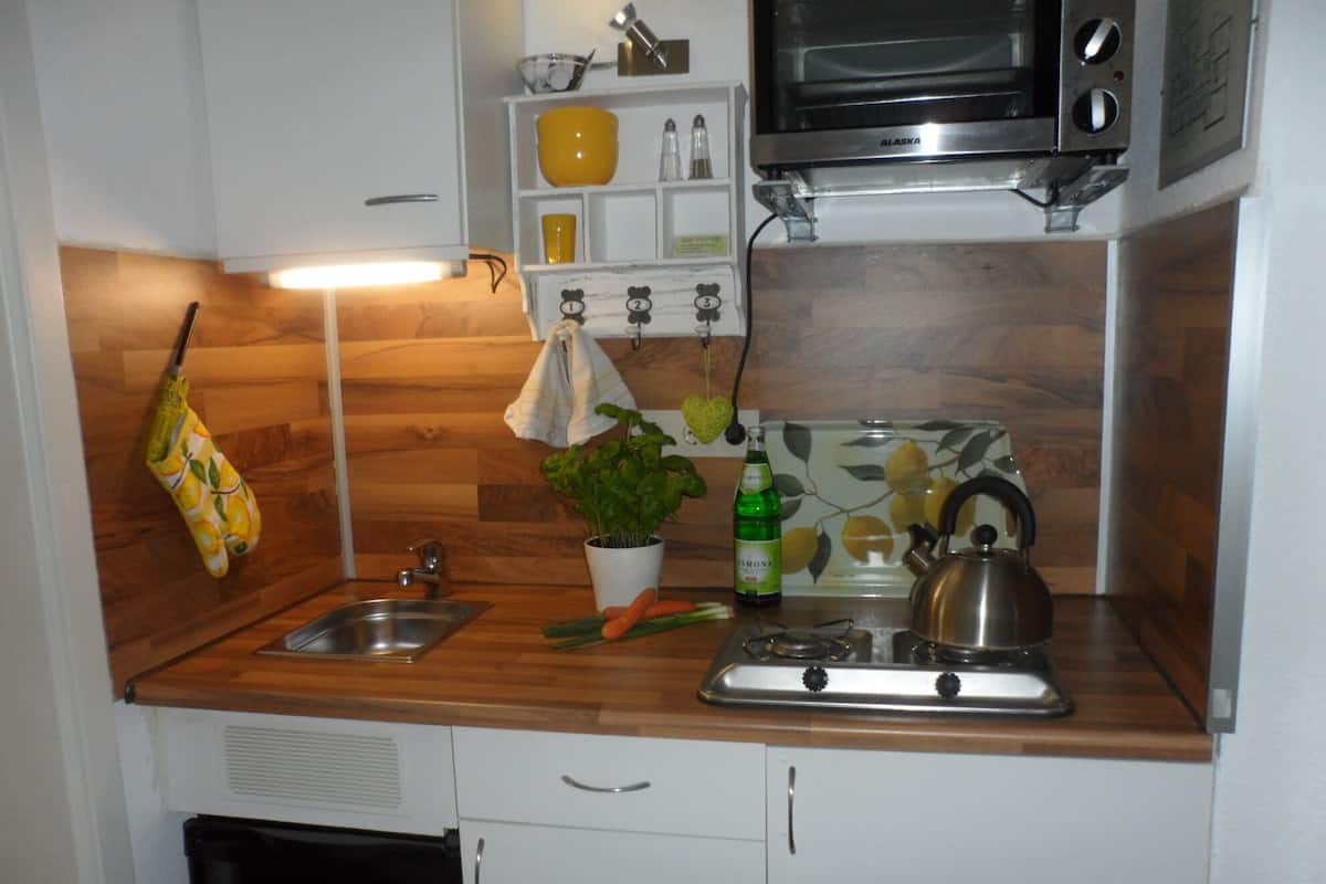 A compact kitchen with a sink, stove, and microwave. There is a plant on the counter and a bottle of beer.