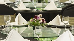 Una mesa de banquete dispuesta con servilletas blancas, platos y cubiertos, y un centro de mesa con flores.