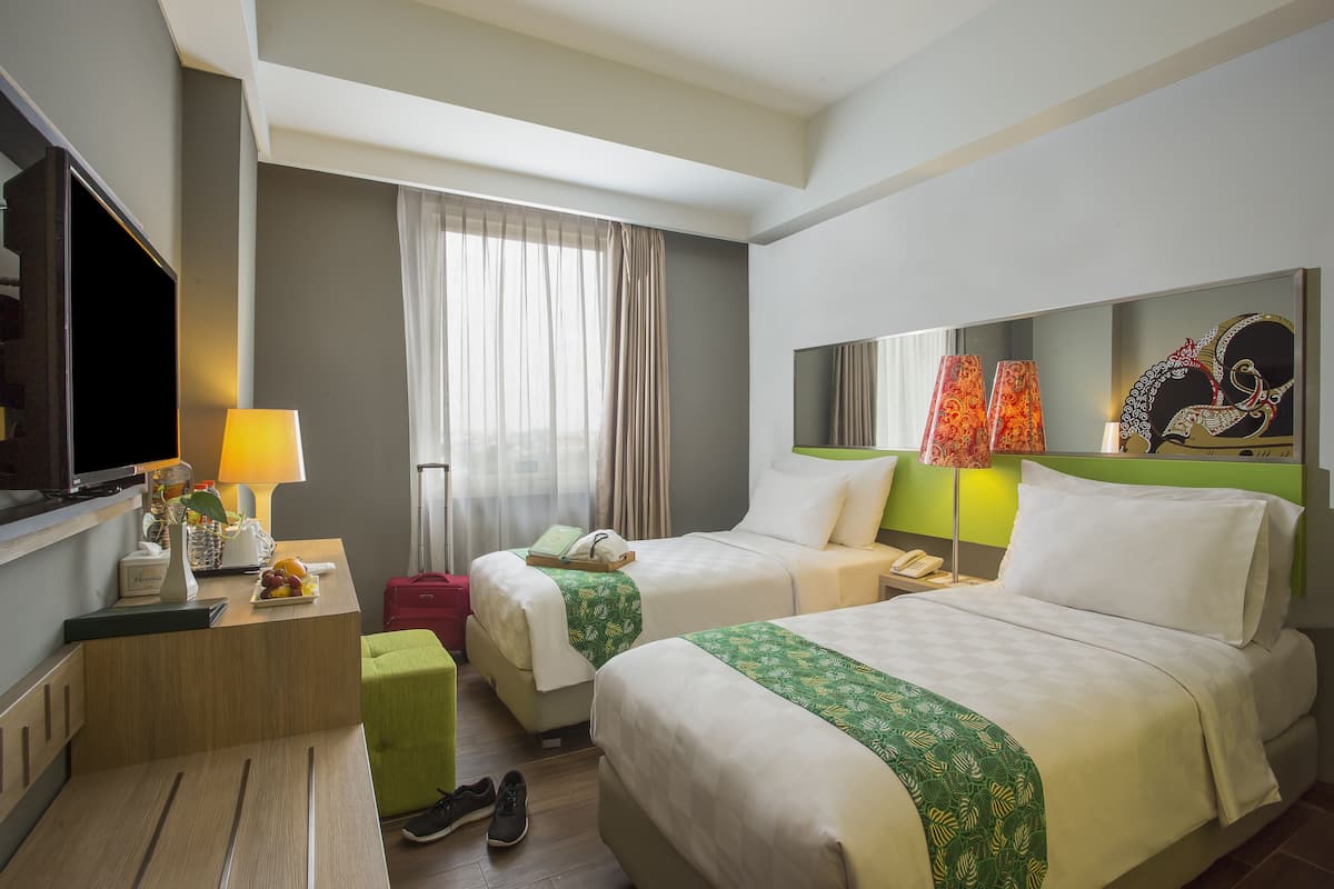 A hotel room with two beds, a desk, a TV, a lamp, and a window with curtains.
